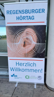 Aufsteller mit der Aufschrift 'REGENSBURGER HÖRTAG' über einem Bild eines menschlichen Ohrs mit grafischen Linien und darunter 'Herzlich Willkommen!'
